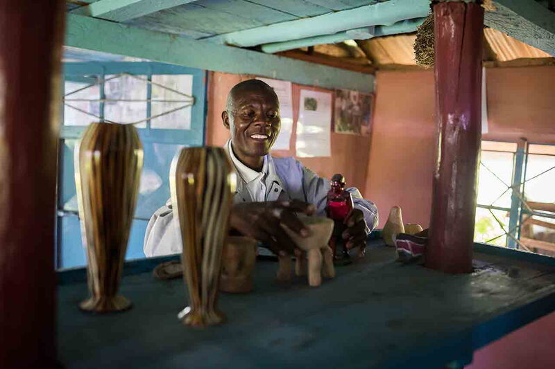 Ein Mann lächelt, während er in seinem Laden handgefertigte Holzfiguren und Vasen arrangiert.