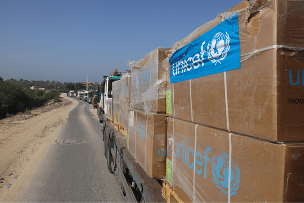 Ein Konvoi von Lastwagen transportiert UNICEF-Hilfsgüter auf einer Landstraße bei sonnigem Wetter.