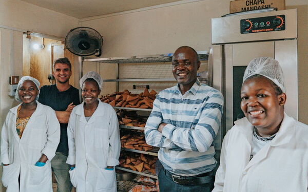 Eine Gruppe von fünf lächelnden Menschen steht in einer Bäckerei neben einer Ladung frischer Backwaren.
