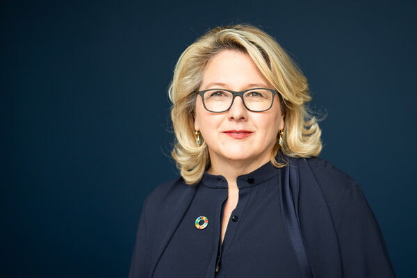 A confident woman wearing glasses poses against a dark blue background.