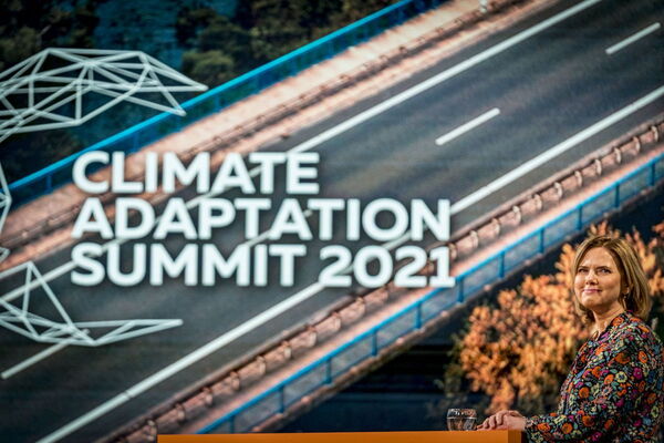 A woman stands on stage at the Climate Adaptation Summit 2021 with a backdrop of a stylized road and geometric design.