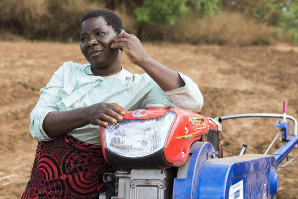 Eine Frau lehnt sich an einen Traktor und telefoniert auf einem Feld, was die Rolle der Digitalisierung in der Landwirtschaft zeigt.