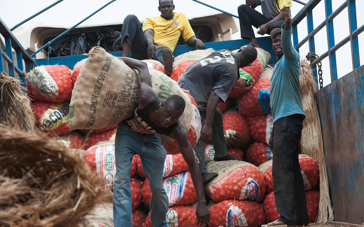 Workers load large sacks of produce onto a truck, showcasing teamwork and effort in the bustling marketplace.