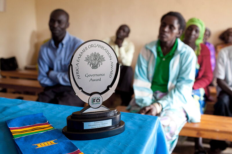 A Governance Award trophy is displayed on a table, with people attentively seated in the background.