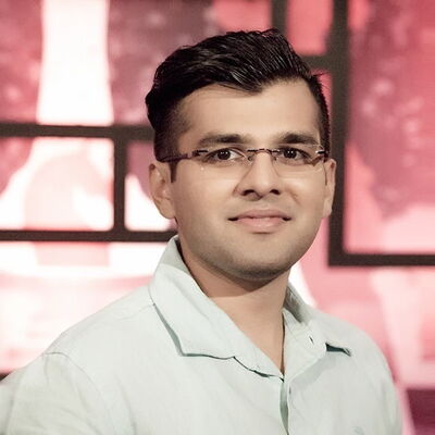A man in glasses and a light shirt smiles against a warm-toned abstract background, conveying a sense of confidence.