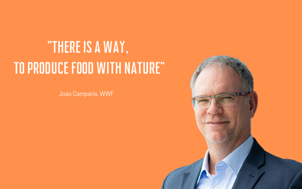 A man in a suit stands against an orange background next to a quote about producing food with nature.
