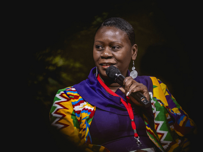 Eine Frau spricht während einer Podiumsdiskussion auf der GIZ Land Week 2025 in ein Mikrofon, gekleidet in bunter Kleidung.