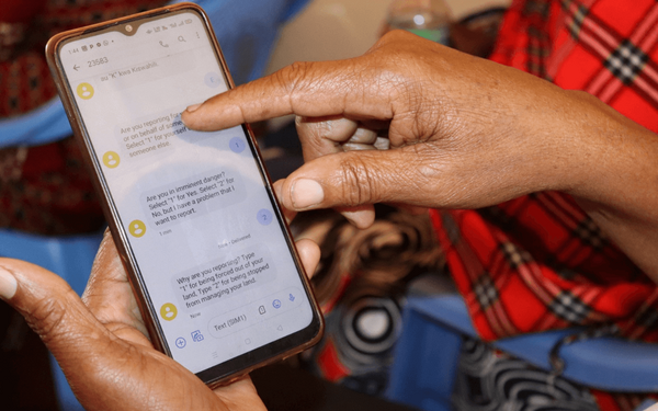 Eine Person zeigt auf ein Smartphone-Display mit einer Textnachricht über Landrechte und Schutzmaßnahmen.