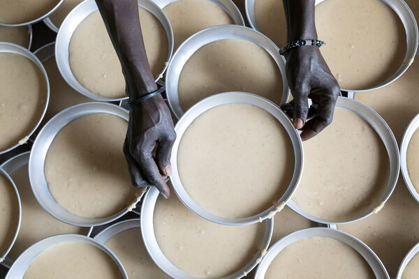 Hands arrange multiple circular molds filled with batter, creating a pattern of preparation and culinary artistry.