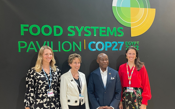 Vier Personen stehen vor dem Schild "Food Systems Pavilion COP27" in Ägypten und lächeln in die Kamera.