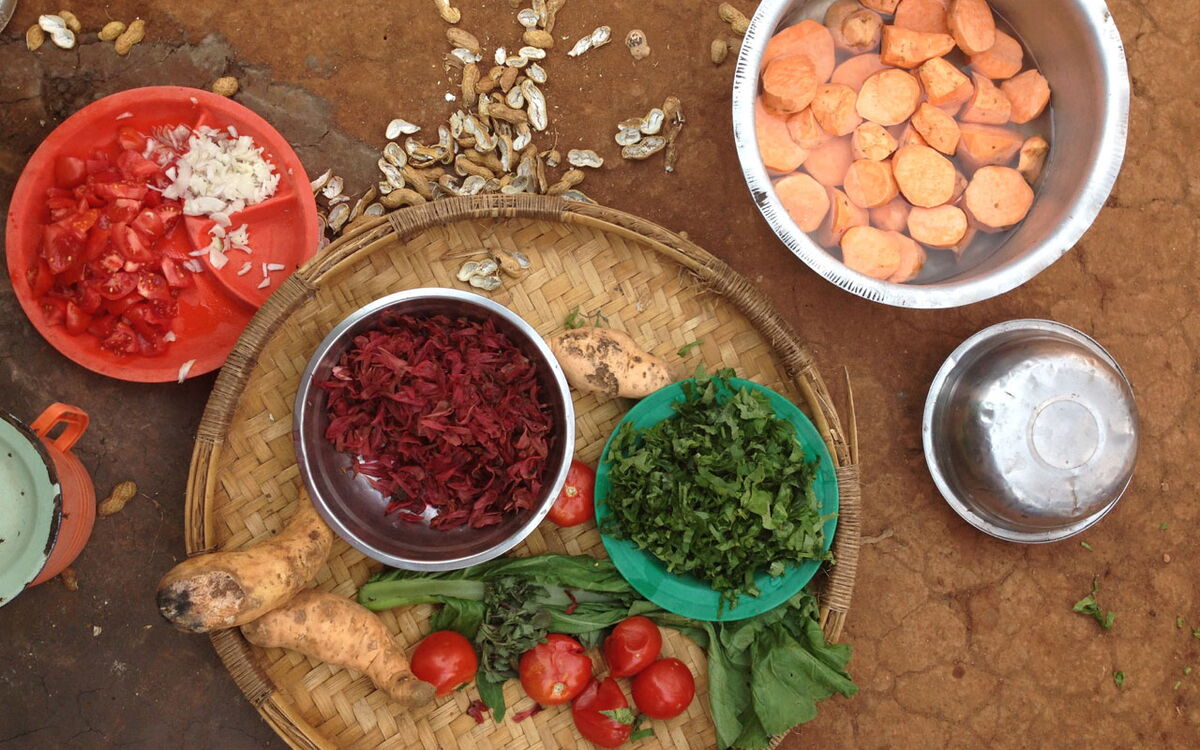 A variety of fresh vegetables and sweet potatoes are arranged in bowls and baskets on the ground in Malawi.