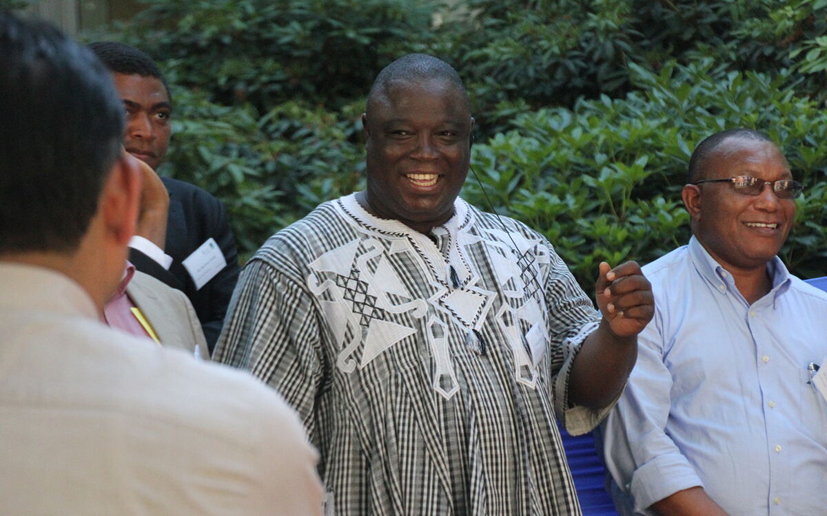 A man in a patterned shirt joyfully engages with a group of people outdoors, surrounded by lush greenery.