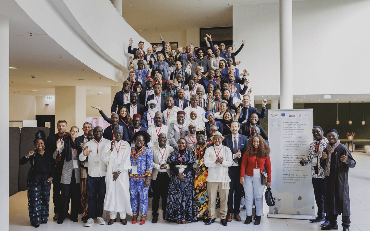 A large group of diverse individuals gathers at Berlin Land Week 2025, smiling and waving in a spacious indoor venue.