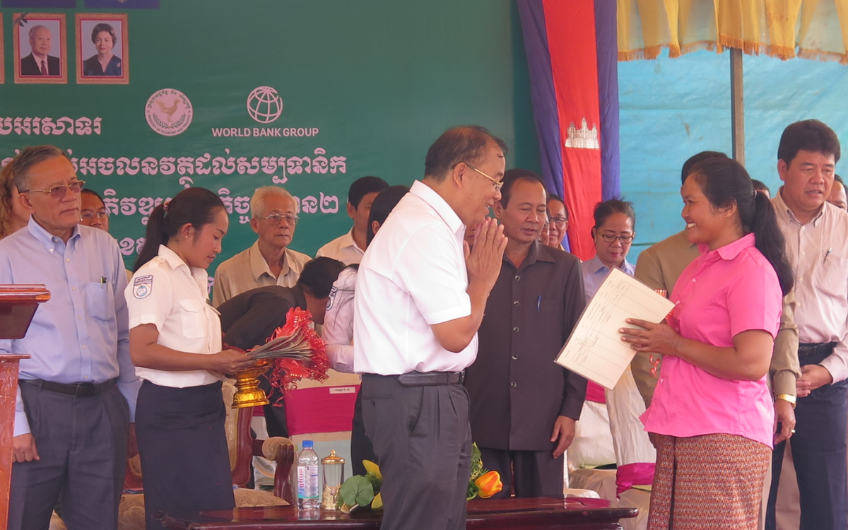 Eine Frau in rosa Hemd erhält vor einer Gruppe von Menschen ein Zertifikat bei einer feierlichen Veranstaltung.
