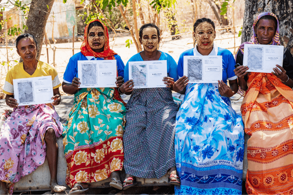 Five women in colorful attire proudly display their land titles in Madagascar, celebrating empowerment and ownership.