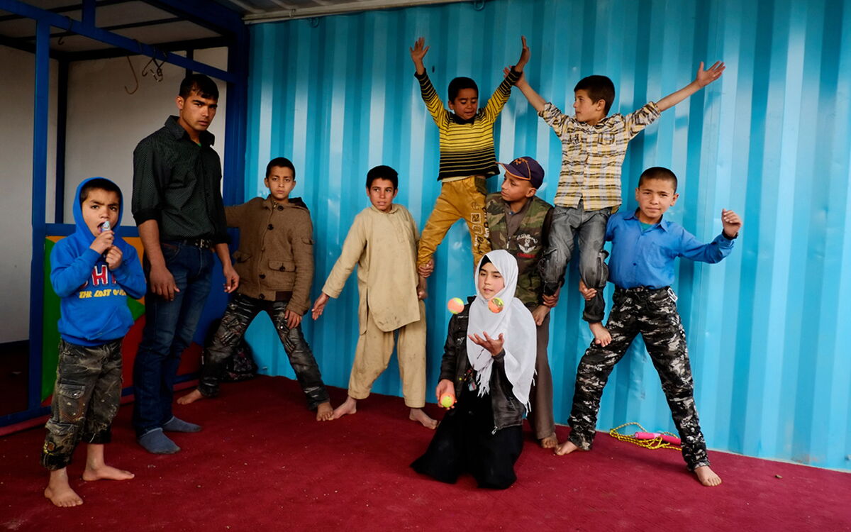 A group of children in colorful clothing play and pose energetically against a vibrant blue background.