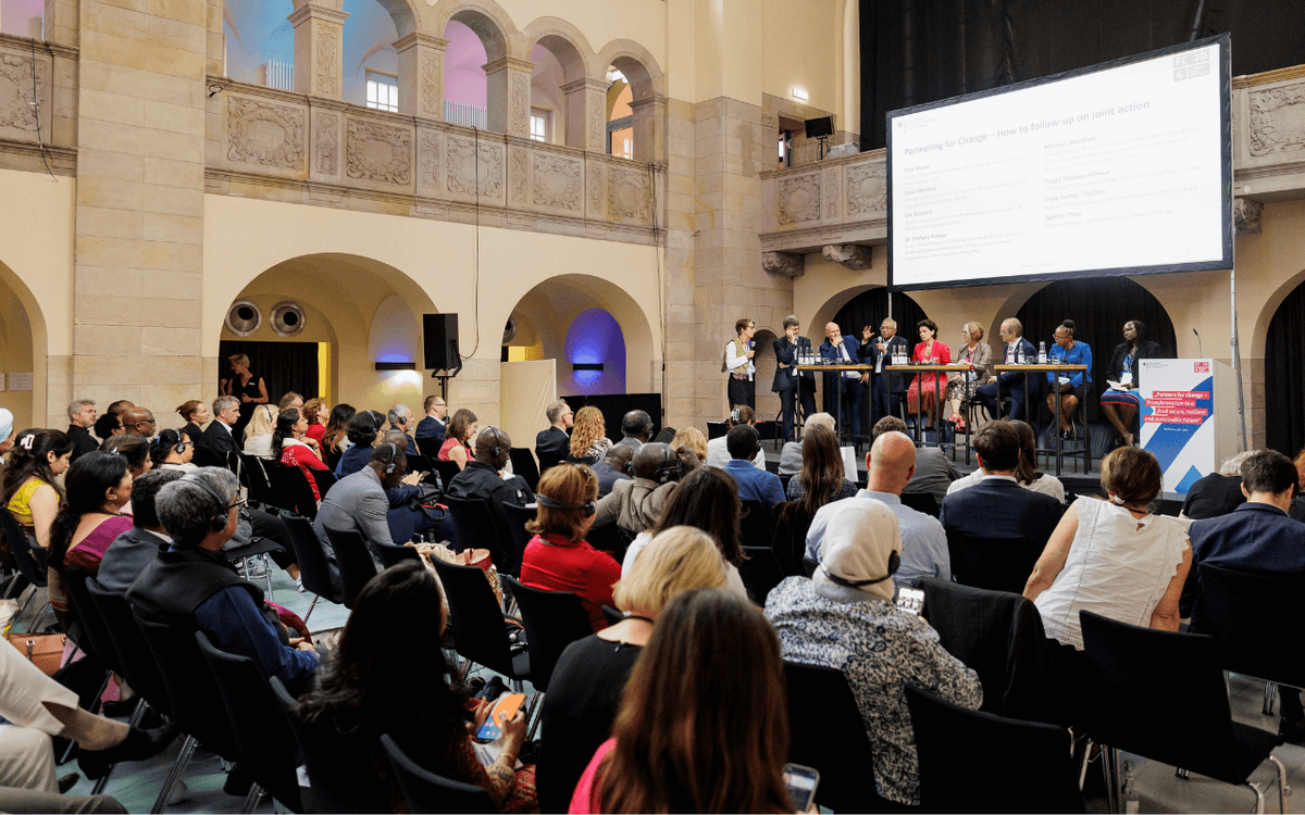 Menschen in einem großen Saal verfolgen eine Podiumsdiskussion über Partnerschaften für Veränderung.
