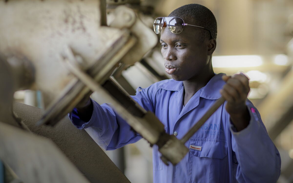 Ein Mann in blauer Arbeitskleidung bedient konzentriert eine große Maschinensteuerung in einer Fabrikumgebung.