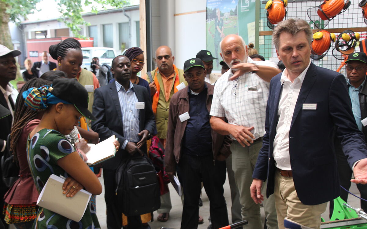 Eine Gruppe von Menschen versammelt sich um zwei Männer, die eine Präsentation über landwirtschaftliche Ausrüstung halten.