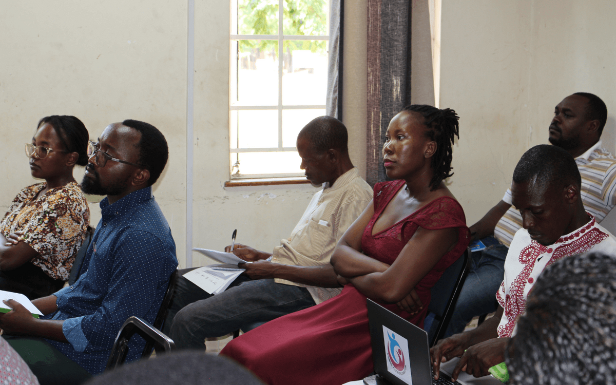 Teilnehmer einer Konferenz hören aufmerksam zu, während sie Notizen machen und einen Laptop verwenden.