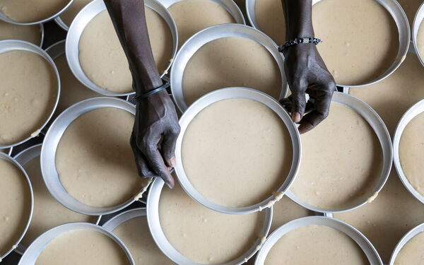 Zwei Hände platzieren Ringe auf gefüllte Backformen, die dicht aneinander gereiht sind.