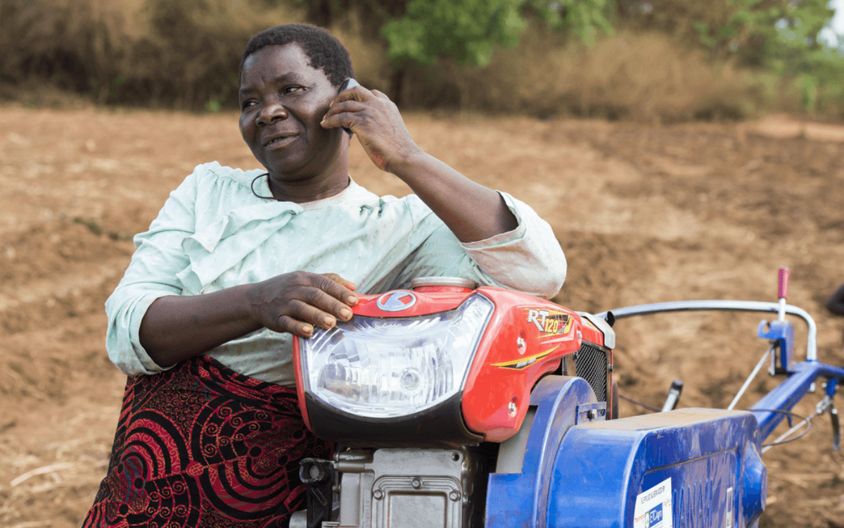 Eine Frau lehnt sich an einen Traktor und telefoniert auf einem Feld, was die Rolle der Digitalisierung in der Landwirtschaft zeigt.