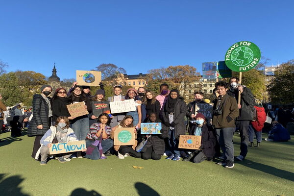 A group of protesters in Stockholm holds climate change signs during a Fridays for Future event in a sunny park.