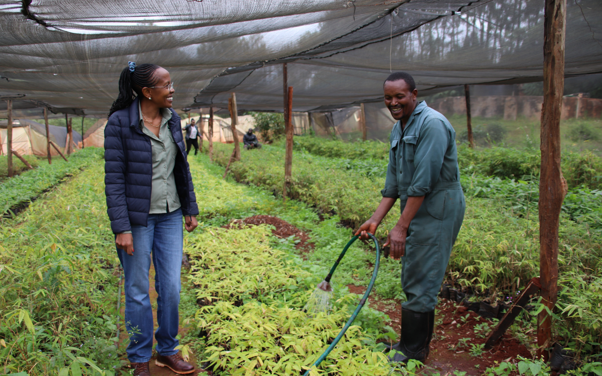 Ein Mann bewässert Pflanzen in einem Gewächshaus, während eine Frau daneben steht und lächelt.