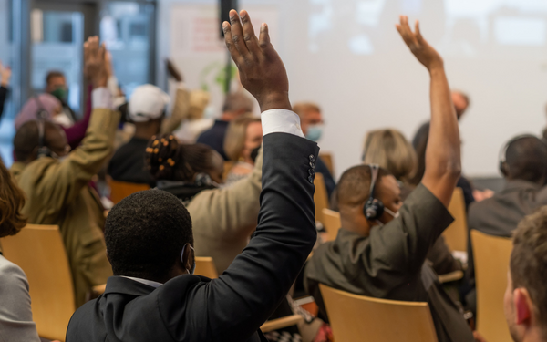 Teilnehmer einer Konferenz heben die Hand, um sich an einer Diskussion über die Gestaltung von Lebensmittelsystemen zu beteiligen.
