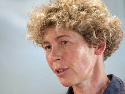 A person with curly hair is speaking passionately in a close-up shot.