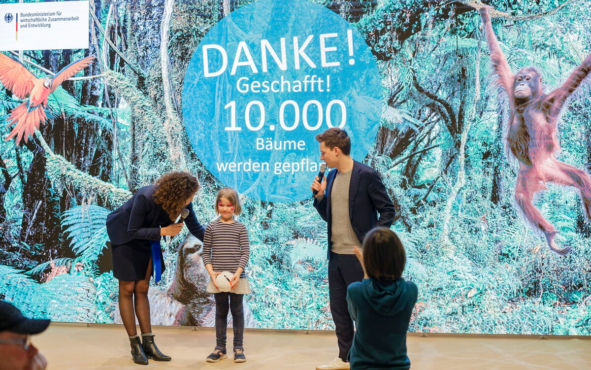 Eine Frau und ein Mann feiern den Abschluss der Challenge "10.000 Bäume in 10 Tagen" vor einem großen Waldhintergrund.