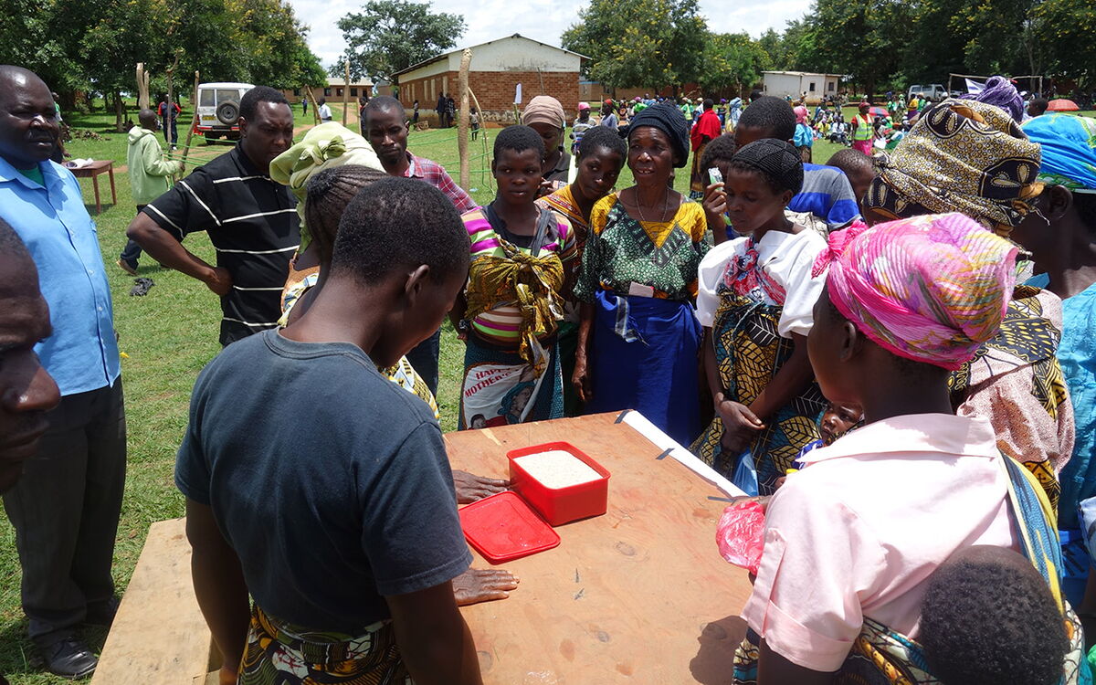A group of people in Malawi gather around a table during a community event, engaging in a discussion.