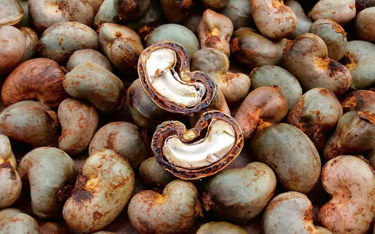 A pile of raw cashew nuts with one split open to reveal the creamy interior, highlighting their natural texture.