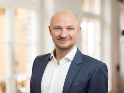 A man in a blue suit stands confidently in a bright room, embodying the spirit of fairness and professionalism.