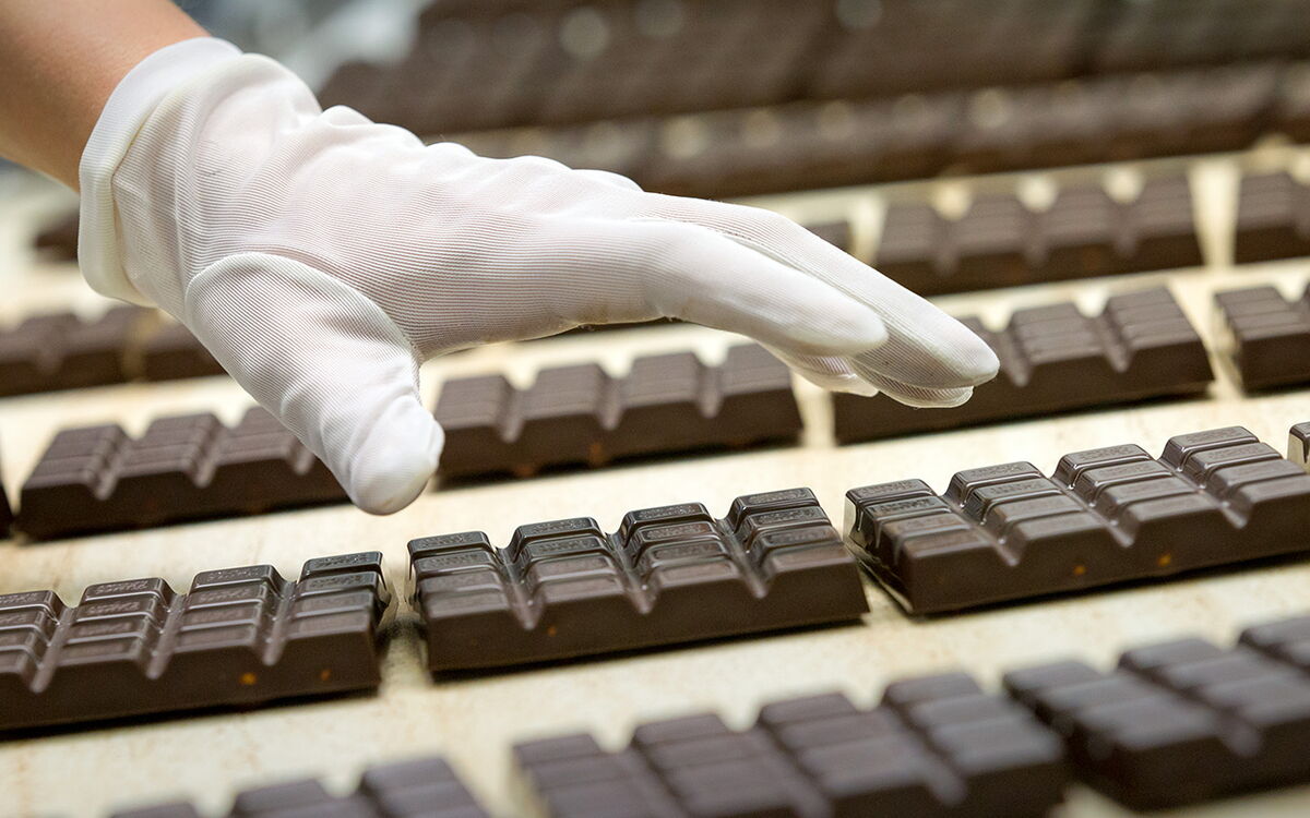 Eine behandschuhte Hand überprüft sorgfältig die Qualität von Schokoladen auf einem Produktionsband.