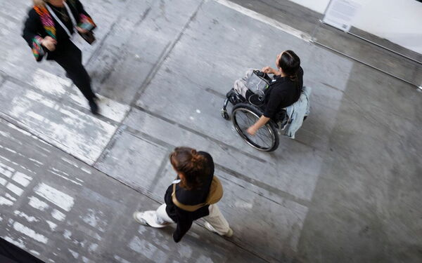 Menschen, darunter eine Person im Rollstuhl, bewegen sich auf einem grauen Boden und symbolisieren Inklusion in Agrarwertschöpfungsketten.