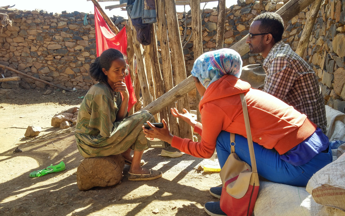 Drei Personen führen draußen in Äthiopien ein intensives Gespräch neben einer Steinmauer.