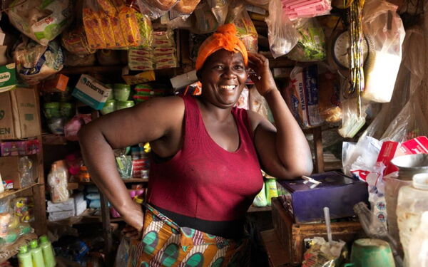 Eine lächelnde Frau steht in einem bunten Laden voller Waren und repräsentiert wirtschaftliche Gleichheit.