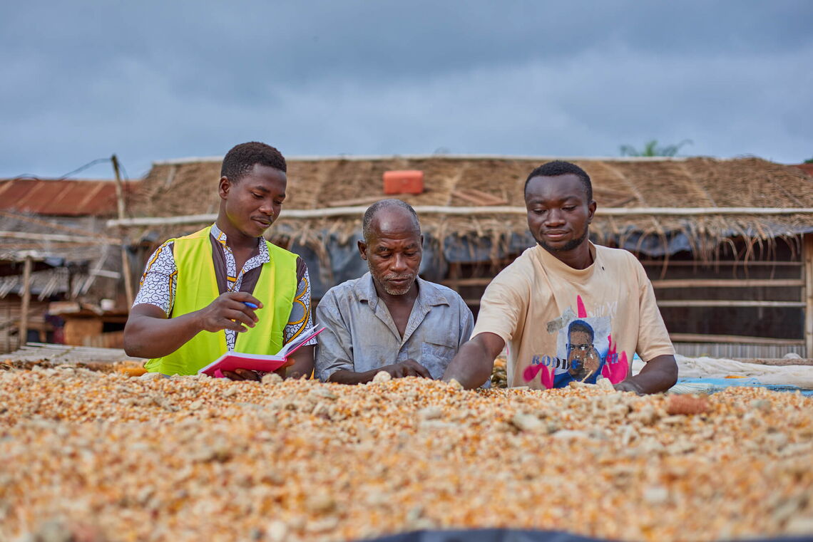 A cooperatives coach discusses land ownership documentation benefits with a father and son at a corn drying area.